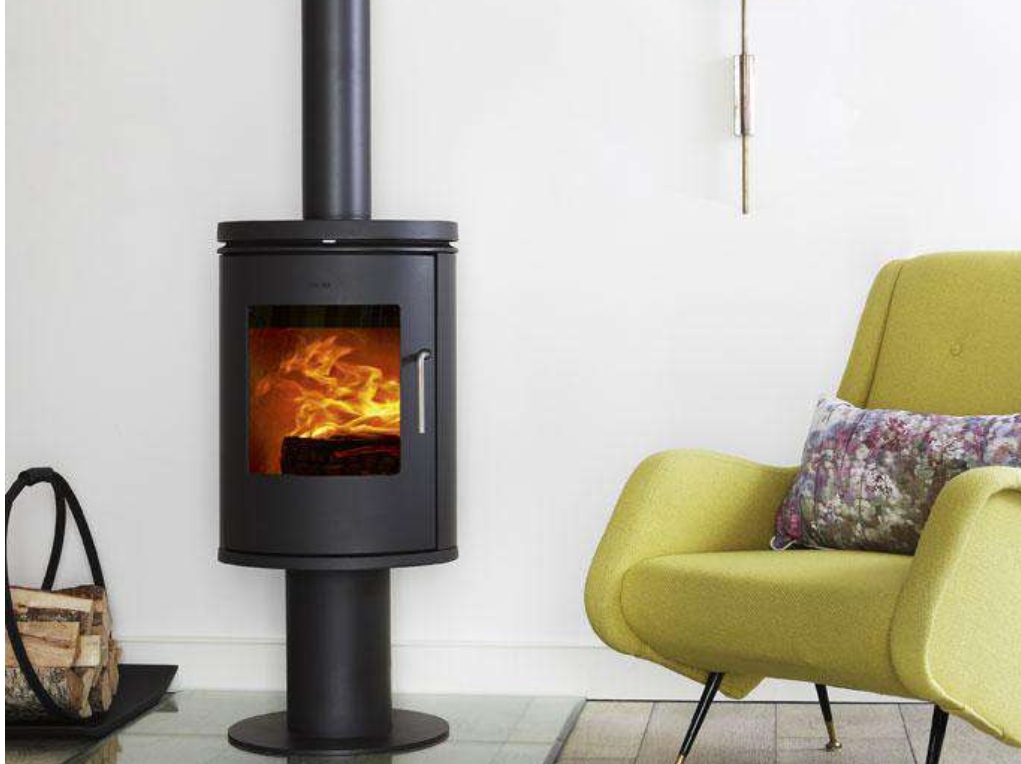 a styling wood burning stove cozily alight nect to a pile of logs. To the left is a green armchair